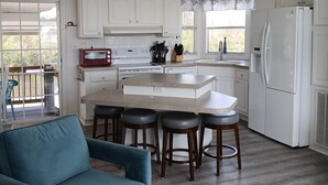 A modern kitchen with white cabinets, a central island with stools, a refrigerator, and a blue sofa in the living area.