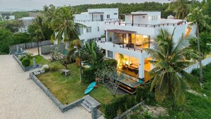 A modern multi-story house with a pool, surrounded by lush greenery and palm trees. - Peaceful Beachfront Pool Villa – Kui Buri (Bangkok Bo Nok, Kuri Buri)