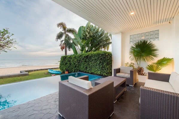Un espacio al aire libre techado con piscina, mobiliario de mimbre y vistas a la playa.