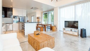 A modern living room with a TV, wooden furniture, and a kitchen area in the background. - Peaceful Beachfront Pool Villa – Kui Buri (Bangkok Bo Nok, Kuri Buri)