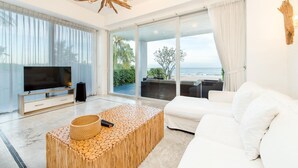 A modern living room with a large TV, white sofa, and a view of the ocean. - Peaceful Beachfront Pool Villa – Kui Buri (Bangkok Bo Nok, Kuri Buri)