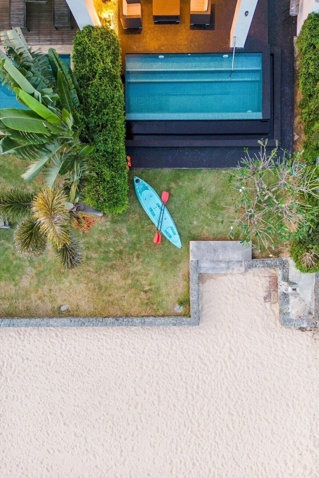 Vue aérienne d’un espace piscine avec un kayak et une pagaie, entouré d’une végétation luxuriante et d’une plage de sable.