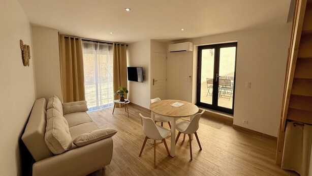 Ein Wohnzimmer mit einer Couch, einem Esstisch mit Stühlen, einem Fernseher und einer Schiebeglastür nach draußen.
