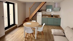 Eine moderne Küche mit Mikrowelle, Spüle und Schränken. Es gibt einen Essbereich mit Tisch und Stühlen. Eine Treppe führt auf eine obere Ebene.