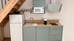 Eine kompakte Küche mit einem weißen Kühlschrank, einem Waschbecken mit goldfarbener Armatur, einer Kaffeemaschine und einer Mikrowelle.