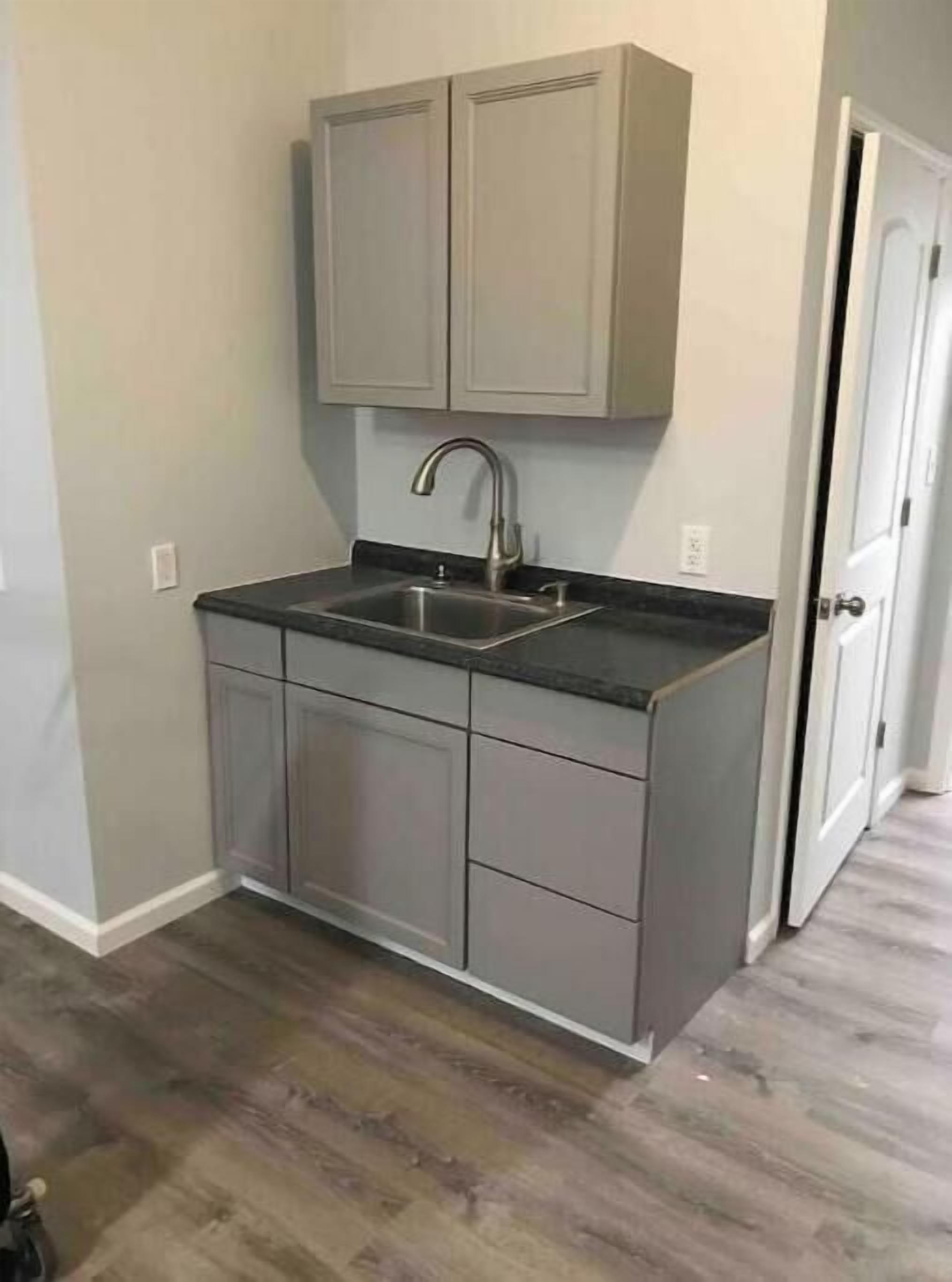 A kitchen with a built-in sink, grey cabinets, and a wooden floor.