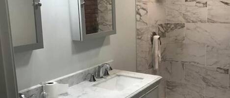 Une salle de bain avec deux lavabos, un miroir, un porte-serviettes et un espace douche.
