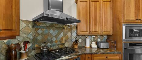 A kitchen with wooden cabinets, a gas stove, a stainless steel range hood, a tiled backsplash, and modern appliances.