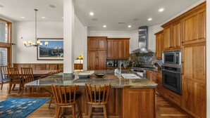 A spacious kitchen with wooden cabinets, a large island with bar stools, and modern appliances. - Legends - Simply Perfect Elkhorn Retreat (Sun Valley)