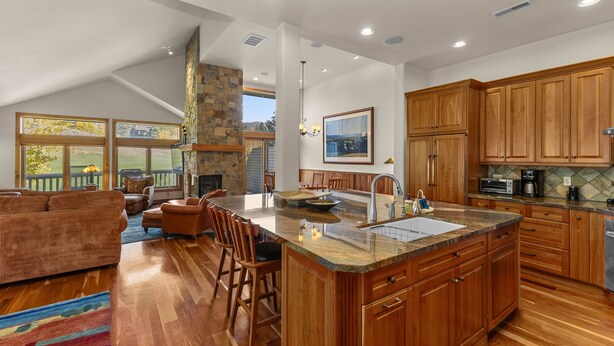 A spacious kitchen with wooden cabinets, a large island with a sink, and a stone fireplace. - Legends - Simply Perfect Elkhorn Retreat (Sun Valley)