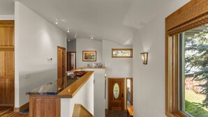 A spacious hallway with a wooden staircase, a dining area, and a view of trees through a large window. - Legends - Simply Perfect Elkhorn Retreat (Sun Valley)