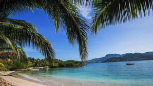 A beach with clear turquoise water, palm trees, and boats. - Charming 1-bedroom apartment at La Ropa Beach (Zihuatanejo)