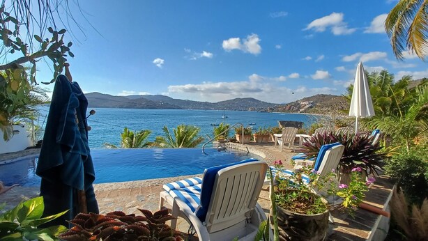 A poolside area with a view of the sea, lounge chairs, and potted plants. - Charming 1-bedroom apartment at La Ropa Beach (Zihuatanejo)