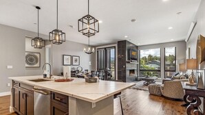 A modern kitchen with a large island, pendant lighting, and a view of the outdoors.