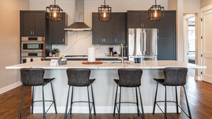 A modern kitchen with dark cabinets, stainless steel appliances, a central island with bar stools, and pendant lighting.