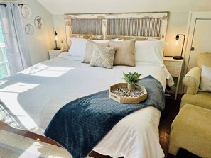 A large bed with a wooden headboard, a bedside table with a lamp, and a chair. - Carriage House studio min to ECU (Ada)