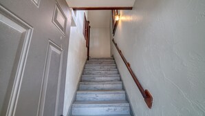 A staircase with white walls and a wooden handrail, leading to a door with a light fixture above it. - Carriage House studio min to ECU (Ada)