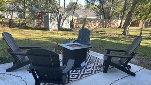 Een terras buiten met twee Adirondack-stoelen en een vierkante tafel, geplaatst op een betonvloer met een geruit kleed.