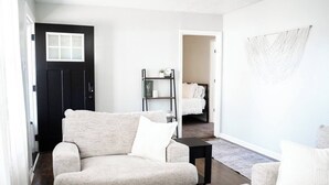 Een moderne woonkamer met een beige bank, een klein zwart bijzettafeltje en een witte wanddecoratie.