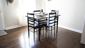 Een eethoek met een donker houten tafel en vier stoelen, een kleine plant op de tafel en decoratieve wandkunst.