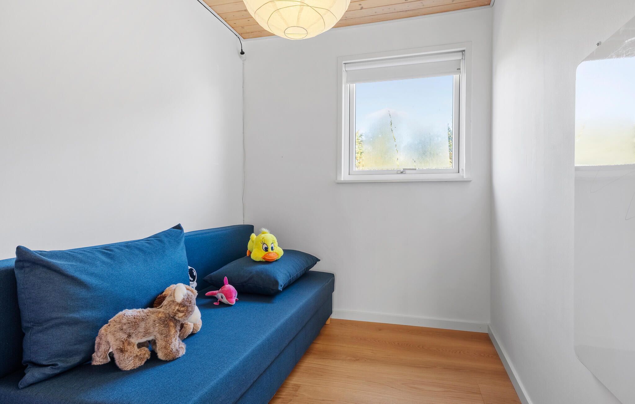 Ein modernes Zimmer mit einem blauen Sofa, einem Fenster mit Blick und einer Holzbalkendecke.