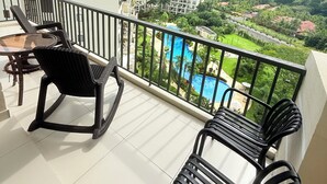 Ein Balkon mit zwei schwarzen Stühlen, einem Glastisch und Blick auf ein von Grünpflanzen und Hochhäusern umgebenes Schwimmbecken.