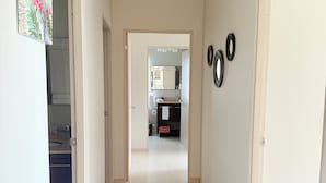 Ein Flur mit Deckenventilator, einer Tür zu einem Badezimmer und einer durch eine offene Tür einsehbaren Küche.