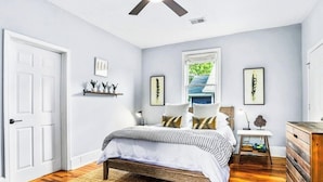 A bedroom with a bed, wooden floor, white walls, a ceiling fan, and a window with a view of greenery. - Stylish Oasis in Prime Location  (Atlanta)