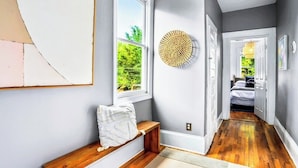 A hallway with a bench, a round woven wall art, and a bed visible through an open door. - Stylish Oasis in Prime Location  (Atlanta)