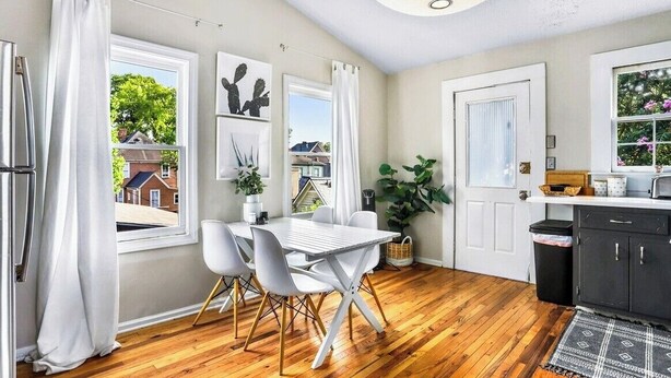 A modern kitchen with a dining area, wooden flooring, white furniture, and large windows with curtains. - Stylish Oasis in Prime Location  (Atlanta)