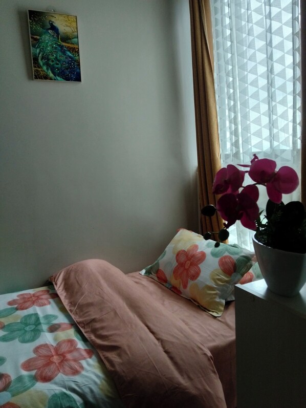 Un dormitorio con una cama, un almohadón estampado con motivos florales, una planta en maceta y un cuadro en la pared.