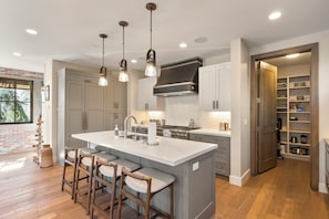 A modern kitchen with a central island, bar stools, pendant lighting, and a built-in oven. - Modern Luxury | 4 BD House | Hot Tub + Sauna (Park City)