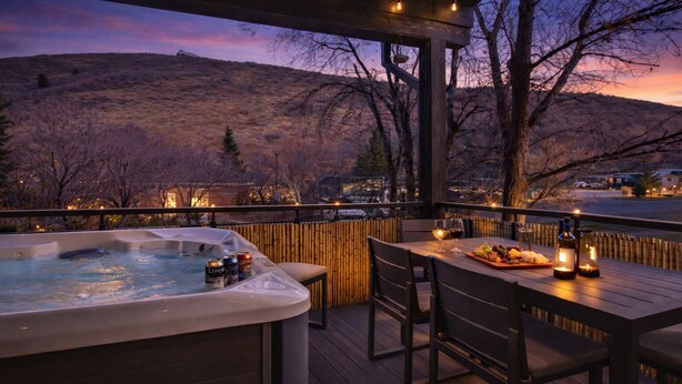 Un jacuzzi en una terraza de madera con una mesa y sillas, con vistas a un paisaje montañoso.