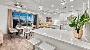 A modern kitchen with white cabinets, a central island, and a dining area with white chairs and a table. - Waterfront Condo with Pool, Spa, and Fitness Center near Downtown Sarasota (Sarasota)