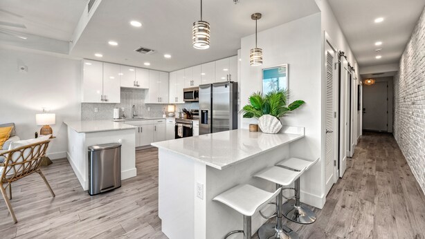 A modern kitchen with white cabinetry, stainless steel appliances, and a central island with bar stools. - Waterfront Condo with Pool, Spa, and Fitness Center near Downtown Sarasota (Sarasota)
