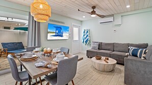 A modern living room with a dining area, grey sofas, a wooden dining table, and a ceiling fan. - CJs - Pet Friendly, Located in Siesta Key Village, Steps to Siesta Key Beach! (Siesta Key)