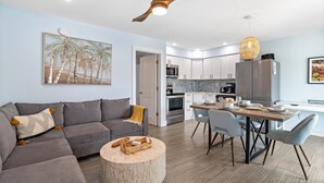 A modern living room with a grey sofa, a wooden coffee table, and a dining area with a wooden table and chairs. - CJs - Pet Friendly, Located in Siesta Key Village, Steps to Siesta Key Beach! (Siesta Key)