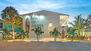 A modern building with a sign reading "CJ's on Siesta" and a staircase leading to an upper level. Palm trees are visible around the building.