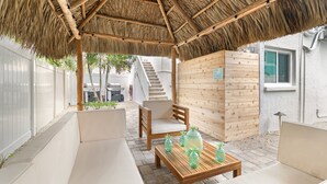 A covered outdoor seating area with wooden furniture and a thatched roof.