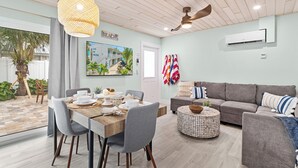A modern living room with a dining area, featuring a wooden ceiling, a ceiling fan, a gray sofa, and a dining table set with plates and bowls. - Sea Dream - Pet Friendly, Located in Siesta Key Village, Steps to Siesta Key Beach! (Siesta Key)