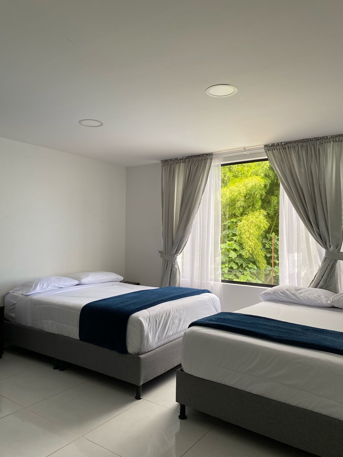 A hotel room with two beds, a large window with curtains, and a ceiling light.