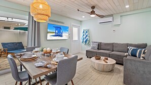 A modern living room with a dining area, a grey sofa, a wooden dining table, and a ceiling fan. - Sea Escape - Pet Friendly, Located in Siesta Key Village, Steps to Siesta Key Beach! (Siesta Key)
