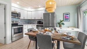 Una cocina moderna con armarios blancos, electrodomésticos de acero inoxidable y una mesa de comedor de madera para cuatro comensales.