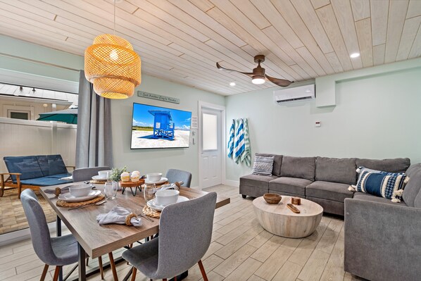 Uma sala de estar moderna com área de jantar, sofás cinzas, uma mesa de jantar de madeira e um ventilador de teto.