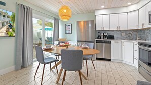 A modern kitchen with white cabinets, stainless steel appliances, and a dining area with grey chairs and a wooden table.