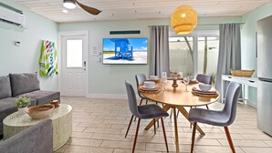 A modern living room with a dining area, featuring a ceiling fan, a flat-screen TV, and a large window with curtains.