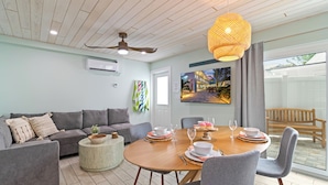 A modern living room with a round wooden dining table, grey sofas, and a ceiling fan.
