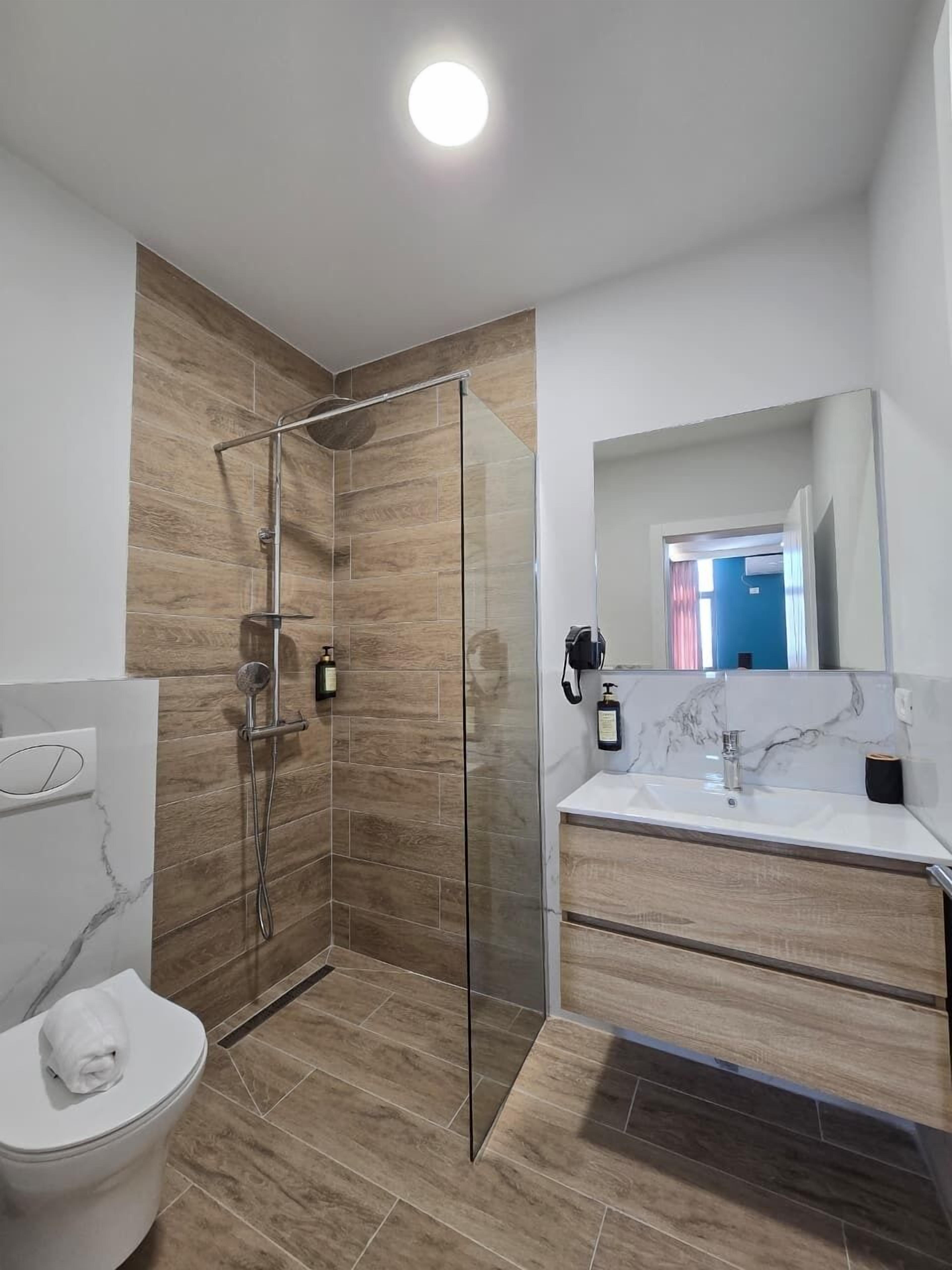 Een moderne badkamer met een douchecabine van glas, een wit toilet en een marmeren wastafel met spiegel.