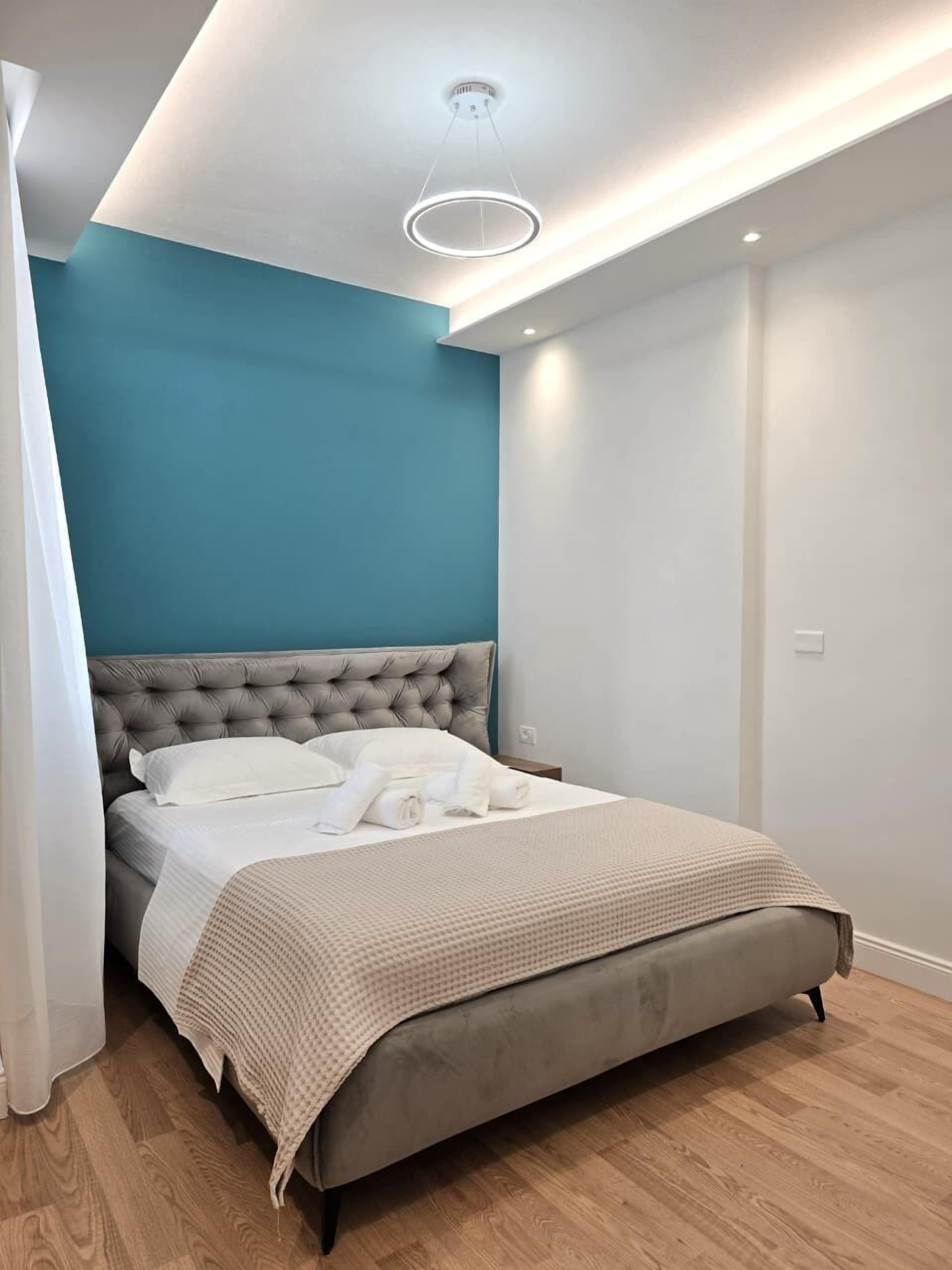 A modern bedroom with a tufted headboard, a neatly made bed with white linens, and a teal accent wall.