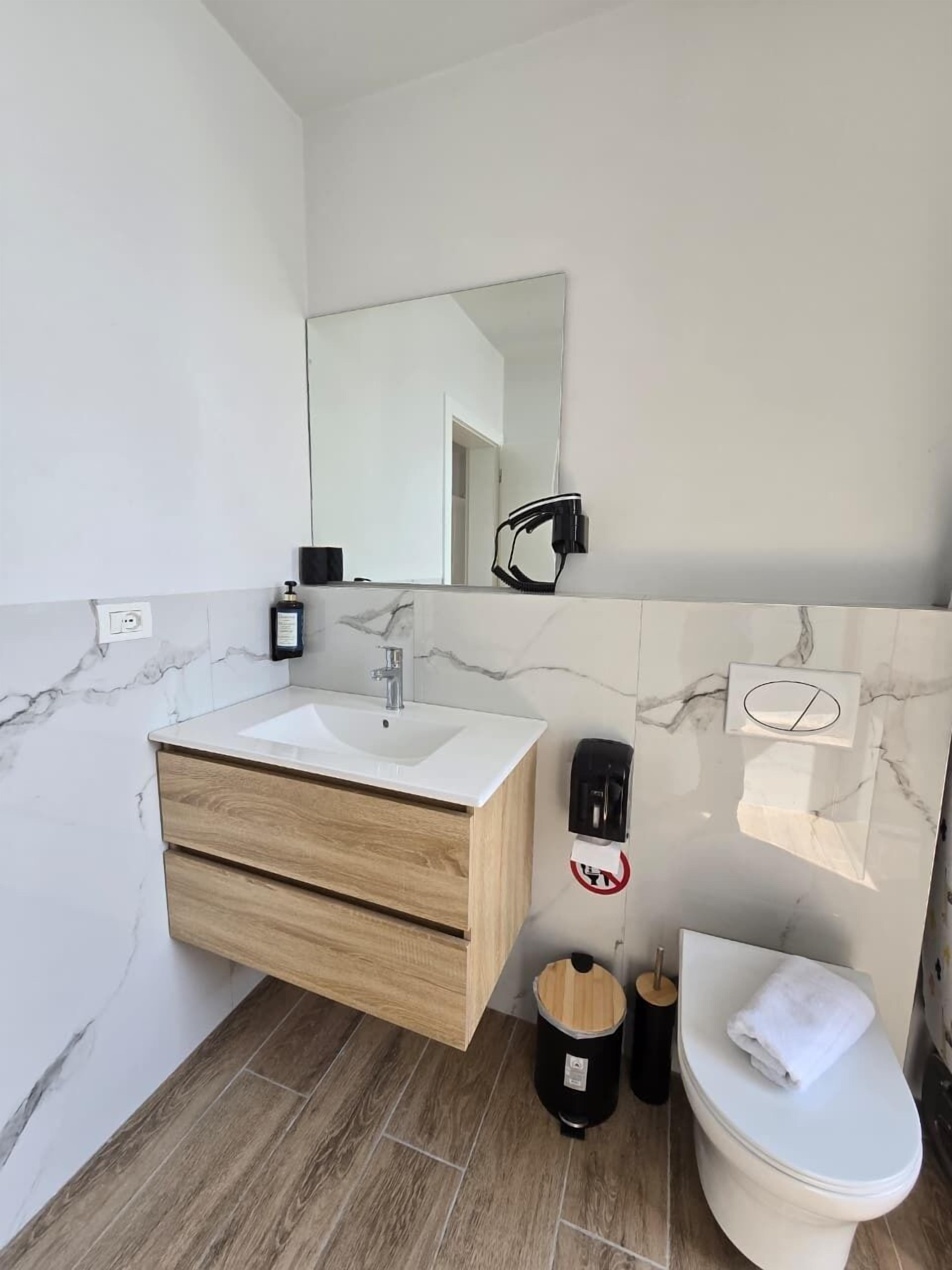 Ein modernes Badezimmer mit Marmorbecken, Holzschrank, Toilette und Spiegel.